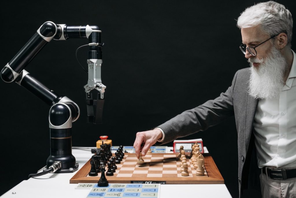 Un uomo che gioca a scacchi contro un braccio robotico, rappresentando la strategia e l'ingegno nell'automazione e nell'IA.
